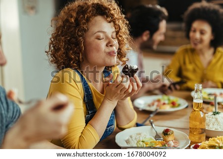 Young woman with eyes closed enjoying in taste of food while eating with friends at dining table.  Royalty-Free Stock Photo #1678004092