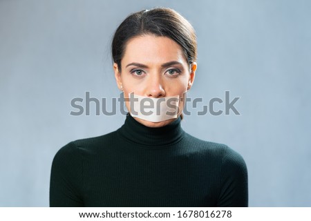 young lady with closed white ribbon mouth, closeup portrait. involuntary silence. censorship Royalty-Free Stock Photo #1678016278