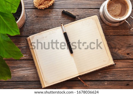 Notebook and coffee, flowerpot, notebook and pen, wooden background, top view. Work at home. Office accessories and office wooden table.