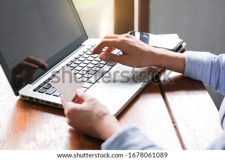 Young women in the office holding plastic credit card and put security code to do online shopping under sunlight. Technology and business concpet.
