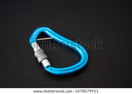 Blue screwgate carabiner locked up, isolated on black background. Centered closeup of locking binner done up. Essential climbing gear.
