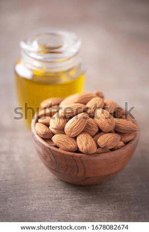 Almond nuts in wooden bowl and almond oil in bottle on wood textured background. Copy space. Superfood, vegan, vegetarian food concept. Macro of almond nut texture, selective focus. Healthy snack