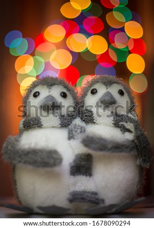 Close up of two penguin figures huddled together in front of christmas lights.