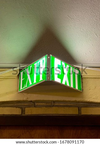 Closeup on an green, glowing Exit sign in an old, urban building.