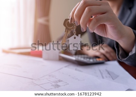 Real estate agent holding house key on table with house designs document,calculator,model house.Concept for real estate Royalty-Free Stock Photo #1678123942