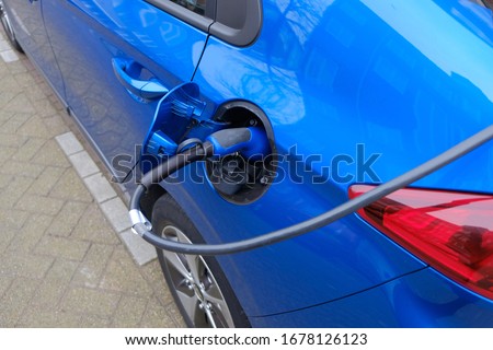 Blue electric car being charged at charging station Royalty-Free Stock Photo #1678126123