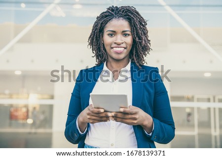 Cheerful professional using app on tablet outside. Young African American business woman holding digital device, looking at camera, smiling. Wi-Fi outside concept