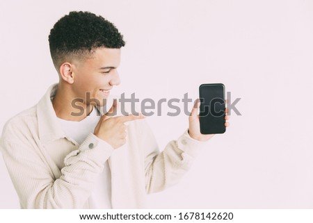 Cheerful young man pointing at smartphone. Handsome happy young man pointing with finger at cell phone with blank screen. Advertising concept