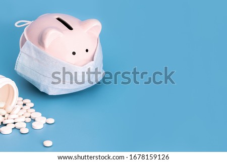 Pink piggy Bank with a medical mask and white pills on a blue background. Coronavirus, 2019-nCoV