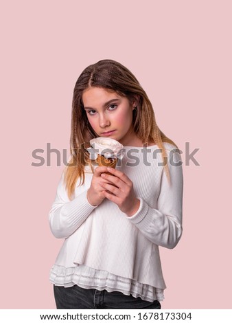 girl in dark gray jeans and a white blouse stands on a pink background and looks directly at the camera