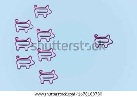 top view of pink piggy paper clips in one direction with leader isolated on purple, leadership concept