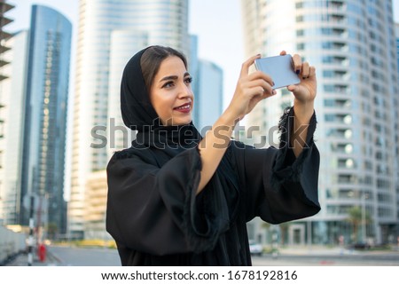 Beautiful muslim middle eastern woman taking photo with mobile phone on the city street.