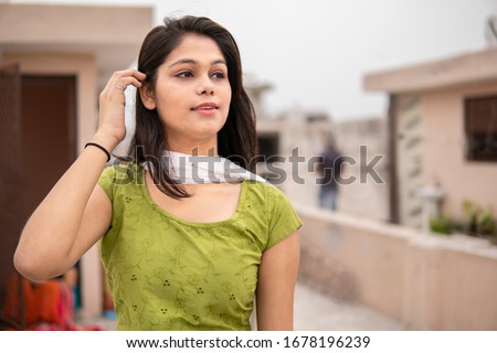 Beautiful, happy Indian late teen girl enjoying fresh air in outdoor at day time. She is looking away and thinking with smile on her face. She is wearing traditional dress salwar Kameez and Dupatta.  Royalty-Free Stock Photo #1678196239