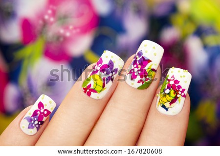 Beautiful multicolored flowers on a white lacquer on the nails on a multicolored background. Royalty-Free Stock Photo #167820608