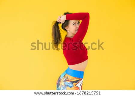 beautiful young girl in leggings performs exercises on a yellow background and smiles