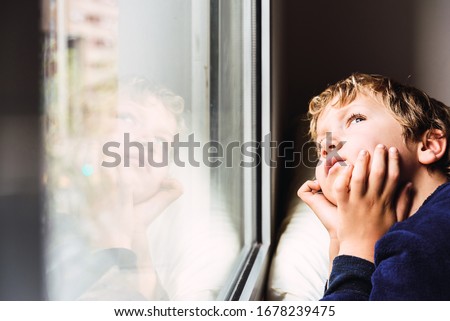 Boy confined at home by the coronavirus crisis in Spain, looks bored out the window without being able to leave home, defocused background. Royalty-Free Stock Photo #1678239475