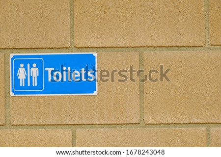 Public toilet sign for restroom with man and woman picture in blue color on a brick wall background