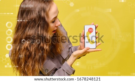 Stylish caucasian girl in a gray dress on a yellow background. A hand holds a smartphone with an icon of a handset and a multitude of not received messages. Close up.
