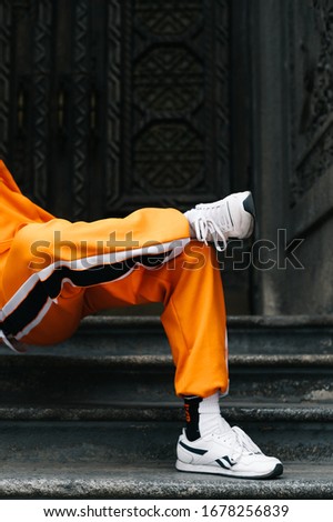 Professional dancer in bright clothes dancing hip hop dance on dark background, cropped, close up photo of legs. Background. Street dancing.Guy in the orange tracksuit dances modern dances.Copy space