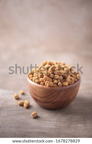 White dried mulberry in wooden bowl on wood textured background. Copy space. Superfood, vegan, vegetarian food concept. Macro of mulberry berries, selective focus. Healthy snack.