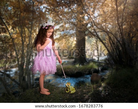 Girl princess casts spell in woods with magic wand on frog wearing crown