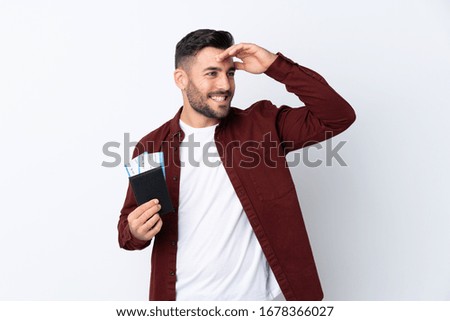 Young handsome man over isolated white background in vacation with passport and plane tickets while looking something in the distance