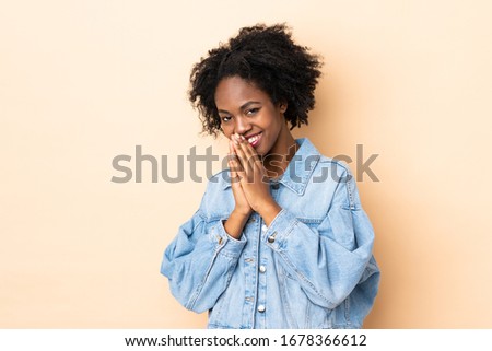 Young African American woman isolated on beige background keeps palm together. Person asks for something