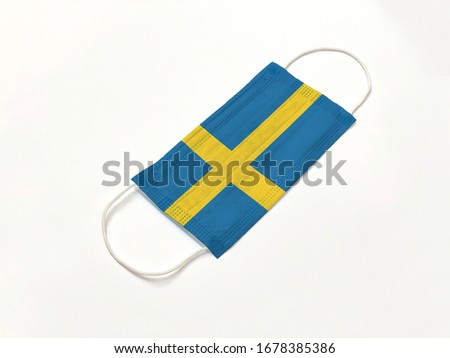 Concept. Conceptual: Disposable medical surgical face mask with Sweden country flag superimposed on it, on white background. Protection against Covid-19 coronavirus outbreak.