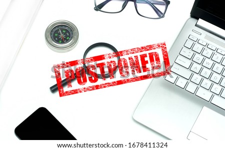 Postponed concept for business meeting, website advertising and others. A roll of paper, compass, smartphone, glasses, magnifying glass and laptop over the white background with "POSTPONED" stamping. Royalty-Free Stock Photo #1678411324