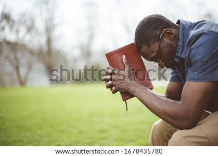 A young African-American male sitting with closed eyes with the Bible in his hands Royalty-Free Stock Photo #1678435780