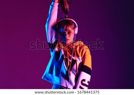 Stylish fashion igen teen hipster pretty girl model wear glasses headphones enjoy listen new trendy dance music mix look at camera hold ponytail stand at purple studio background 80s party, portrait Royalty-Free Stock Photo #1678441375