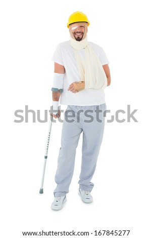Full length of a young man in hard hat with broken hand and crutch over  white background