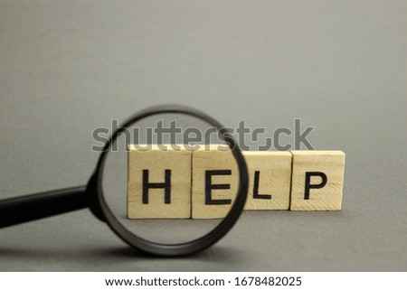 The word Help is made of wooden letters on a gray background