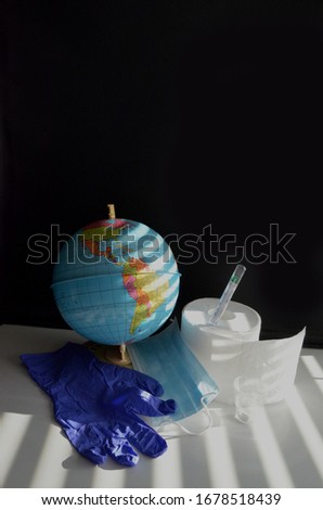 Earth globe America side with the face mask, thermometer, toilet paper roll and blue glove next to the globe. Dark background.