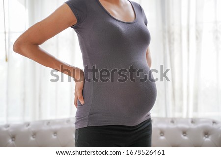 Close Up Picture of a pregnant woman standing with the window in the background at home.