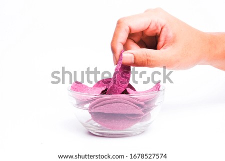 A picture of hand taking purple sweet potato crisps in the bowl