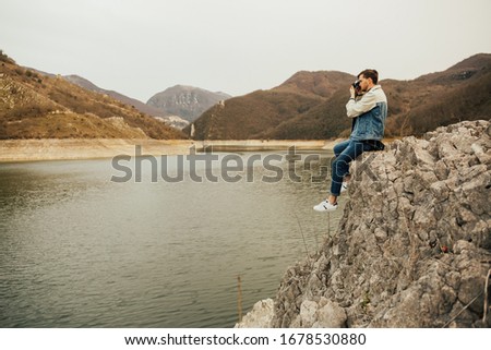 Young man taking picture outdoor. Travel photographer man taking nature photo of mountain and lake landscape in Italy. Professional photographer on adventure vacation.