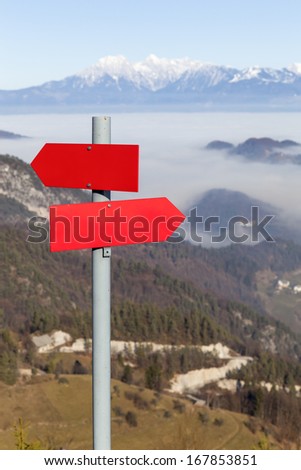 Red mountain guidepost along an alpine pathway over a beautiful landscape in a clear sunny day, space for text