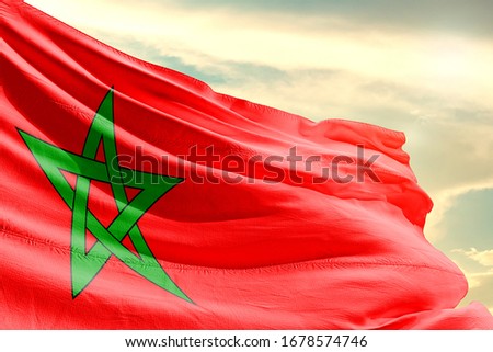 Morocco national flag cloth fabric waving on the sky with beautiful sun light - Image Royalty-Free Stock Photo #1678574746