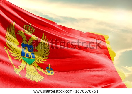 Montenegro national flag cloth fabric waving on the sky with beautiful sun light - Image