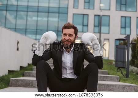 A handsome smiling businessman with a beard in a suit. He wears boxing gloves on his hands
