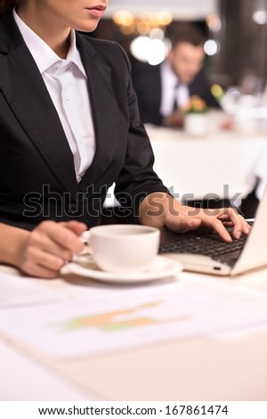 Businesswoman at work. Cropped Image of young woman in formalwear working on laptop and holding a coffee cup while sitting at the restaurant