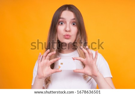 Young cute funny caucasian girl holding a credit card in hands, over isolated yellow background,