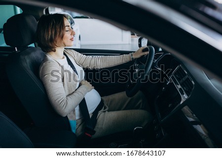 Young pregnant woman testing a car in car showroom