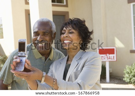 Middle-aged couple photographing in front of new home