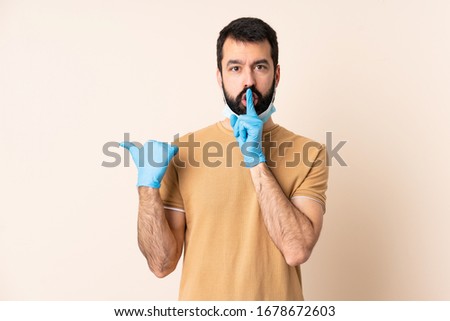 Caucasian man with beard protecting from the coronavirus with a mask and gloves over isolated background pointing to the side and doing silence gesture