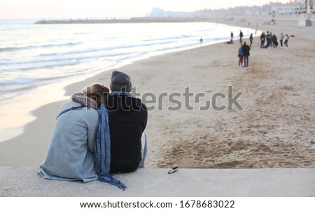 Romantic couple dressed in coats and beanie is meeting beautiful sunset at the seashore/beach. Copy space for message/information. Relaxing during pandemic times. Siges, Spain. Social distancing