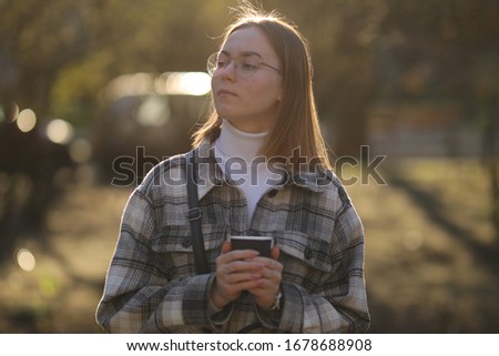 Beautiful girl with blond hair. Girl is drinking coffee in the park. Girl walking on the street, good weather. Girl with glasses drinks hot coffee / tea. Teenager of European appearance
