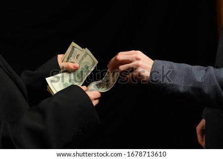 Deal. Arm transfer of money. Female and male hand. Business people transfering dollars on black background.

