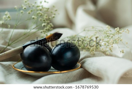 black eggs on a plate with a gold border and a brush on a gray linen background. horizontal photo